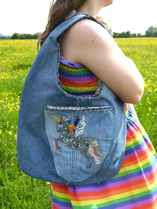 Upcycled denim hobo bag with a sequinned Pegasus appliqué, worn outdoors
